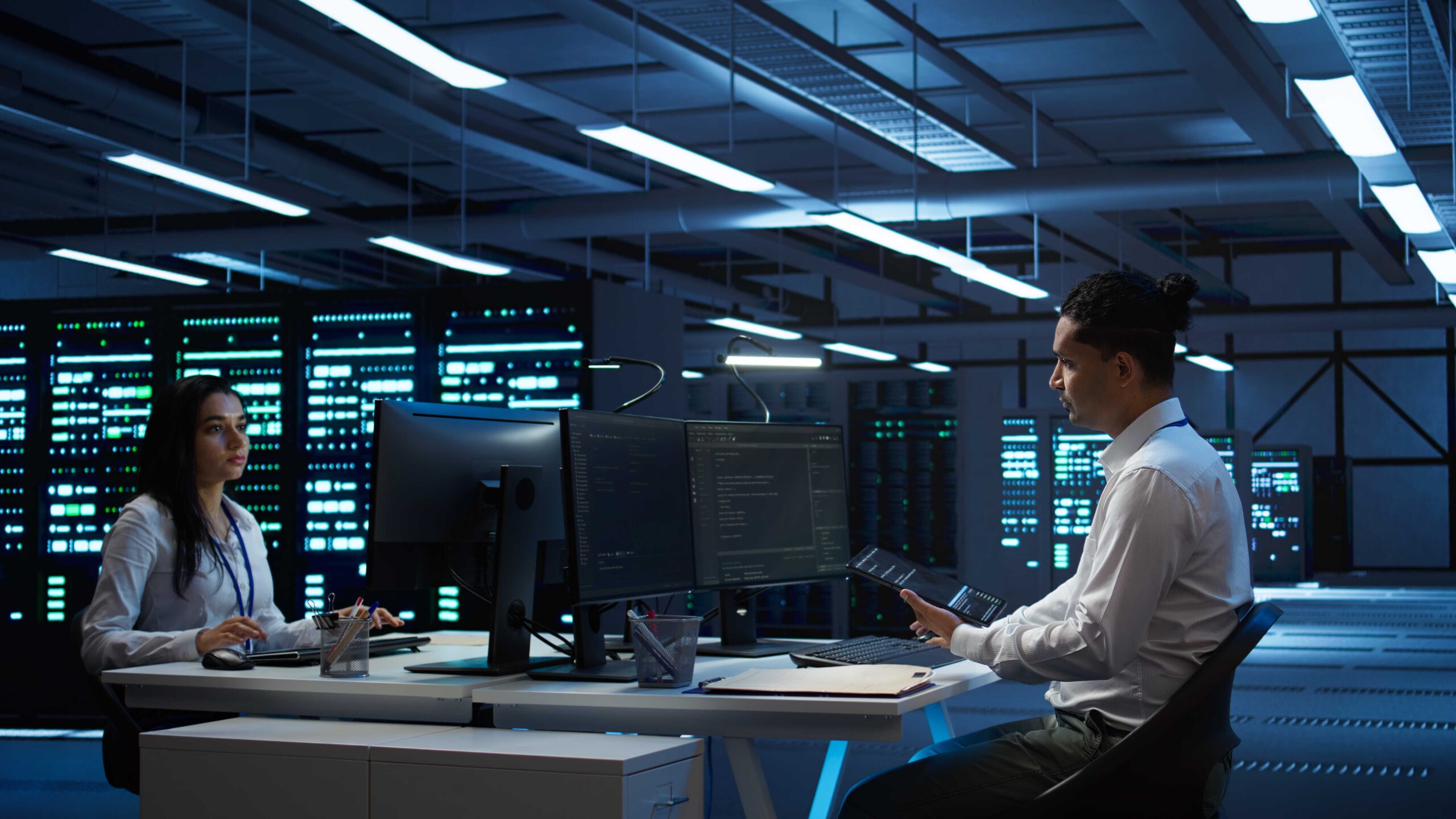 System administrator in data center installing software on computer, troubleshooting issues using tablet. IT staff member in server hub establishing performance benchmarks, camera B